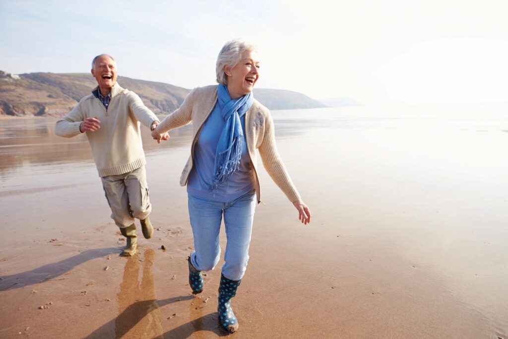 Happy elderly couple running and holding hands on the beach at sunset.